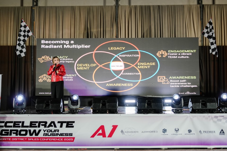 A woman in a red jacket talks on stage, while the screen behind displays a Venn diagram.
