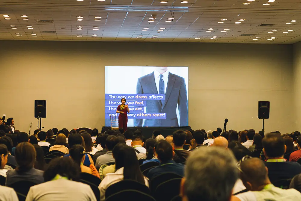A woman in a purple dress presenting a slide in front of a crowd.