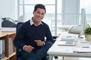 A male officer manager smiling at his desk in a modern office.