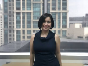 A portrait of a woman in a black dress with a city landscape in the background.