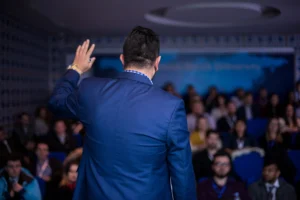 Back view of a male motivational speaker speaking to a crowd.